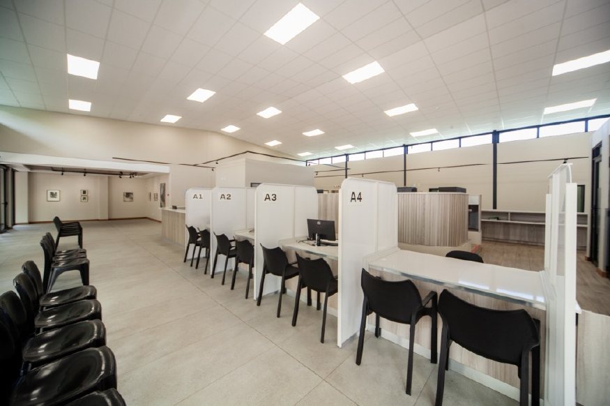Clinic waiting and reception hall with numbered consulting bays, black chairs and a raised glazed management island.