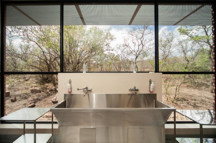 Stainless steel scrub trough in front of a large window looking onto bushveld.