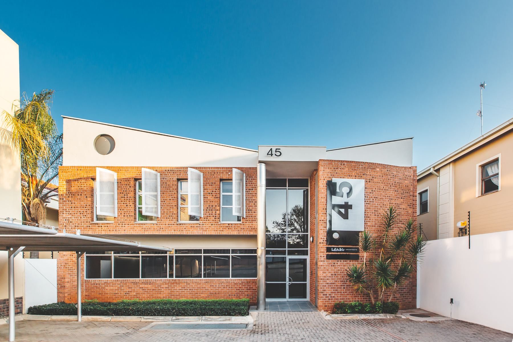 Two-storey face-brick office building with a glazed entrance and the number 45 on a signage panel, under a clear sky.