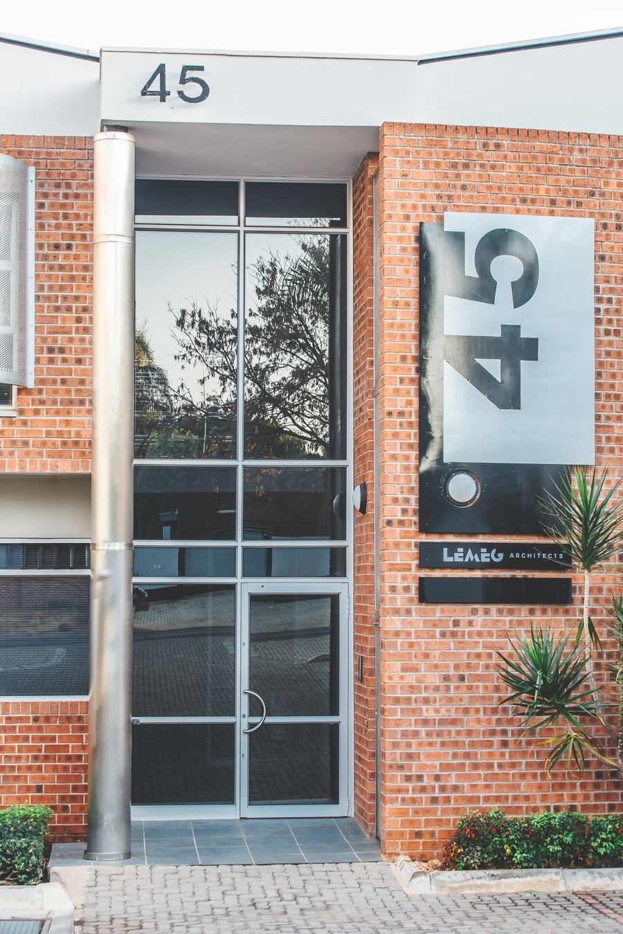Office entrance with a full-height glazed door, a steel column and signage on the face-brick wall.