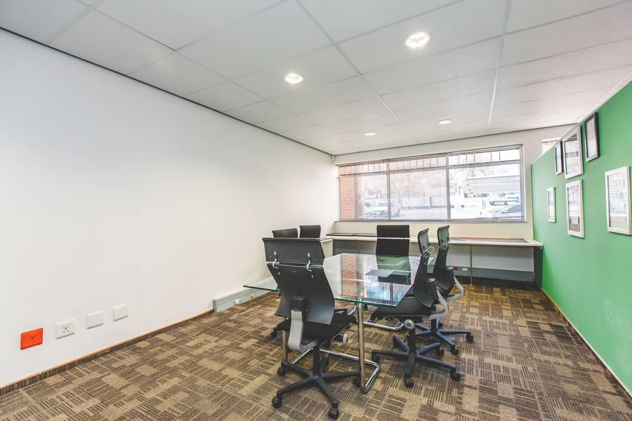 Meeting room with a glass-topped table, black chairs and a green feature wall.