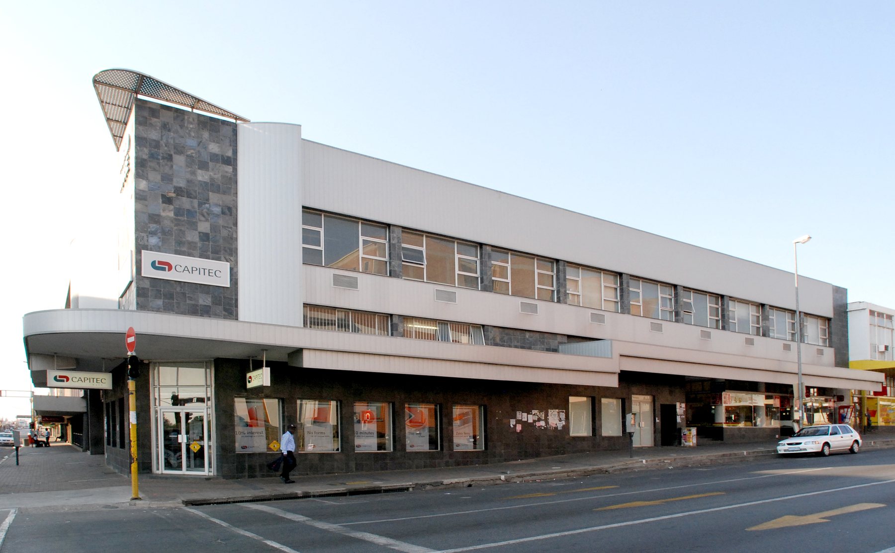 Street view of the corner building with a curved ground-floor canopy, a stone-clad feature and a long first-floor band.