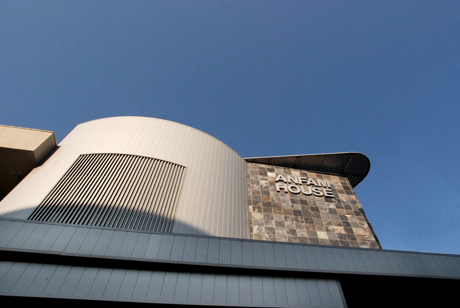 Curved louvred volume and stone-clad feature wall carrying the Anfam House sign, seen from below.