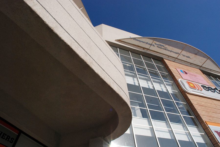 Curved concrete canopy and glazed atrium front with tenant signage, seen from below.