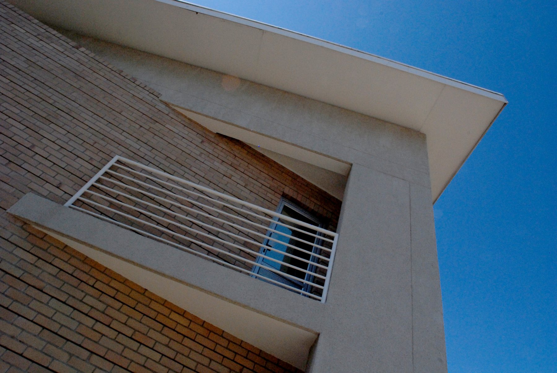 Face-brick wall with a projecting canopy and a steel-railed balcony, seen from below.