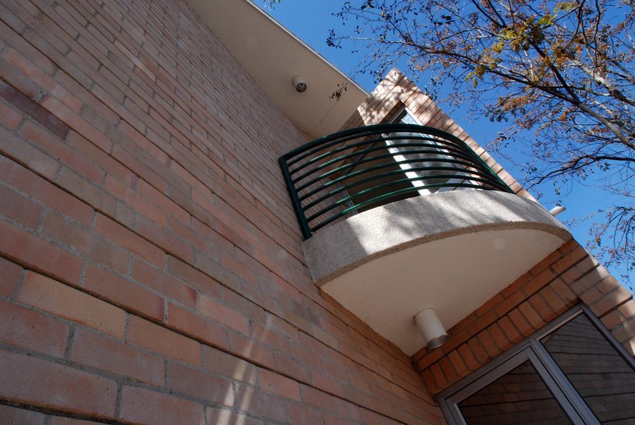 Curved balcony with a green steel balustrade on a face-brick facade.