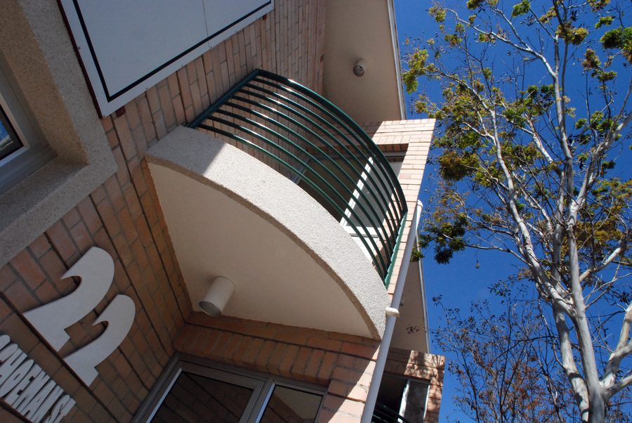 Curved balcony and the number 22 on the face-brick wall, with a tree in front.