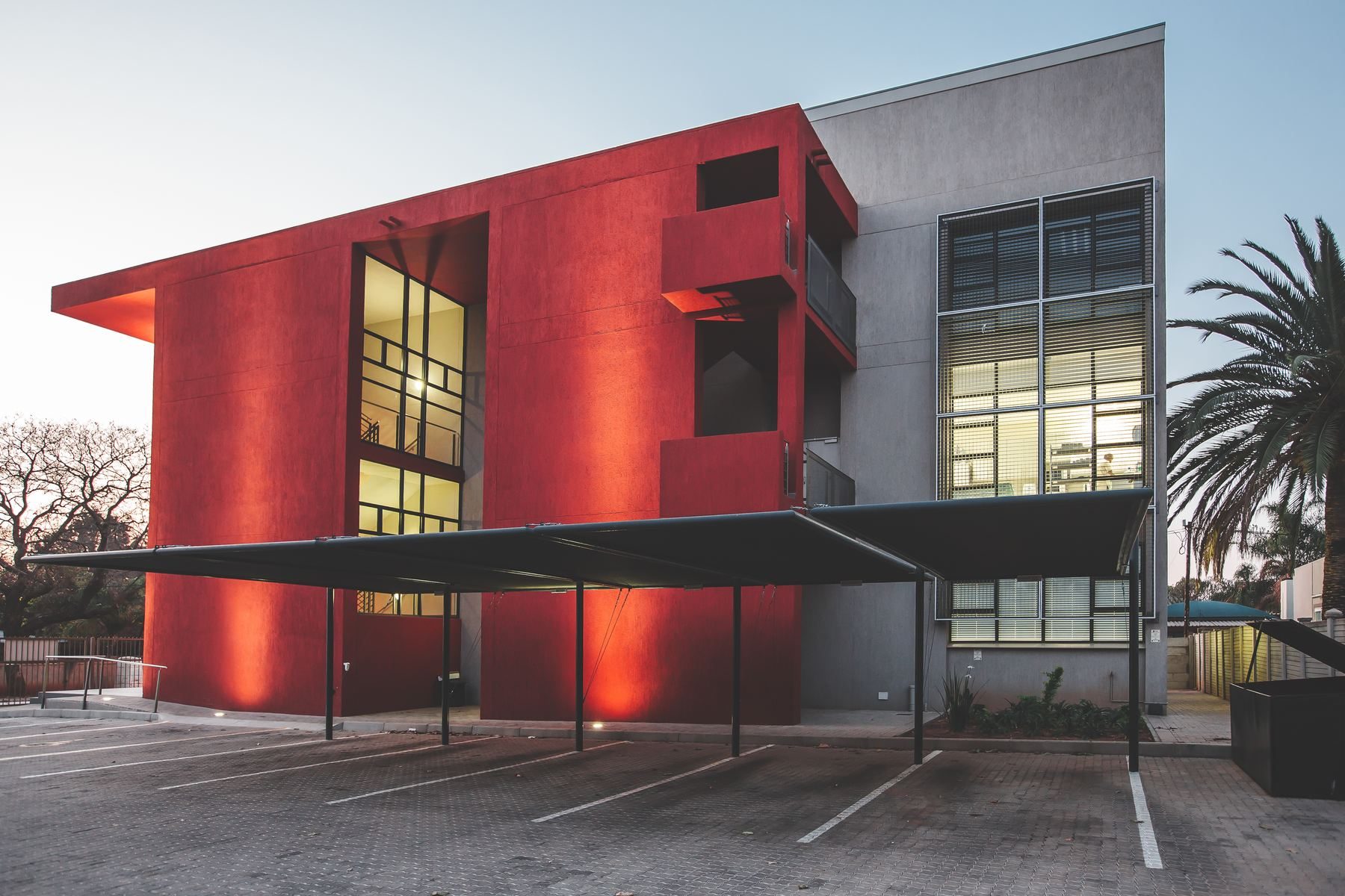 Three-storey red medical building with covered parking, lit at dusk.