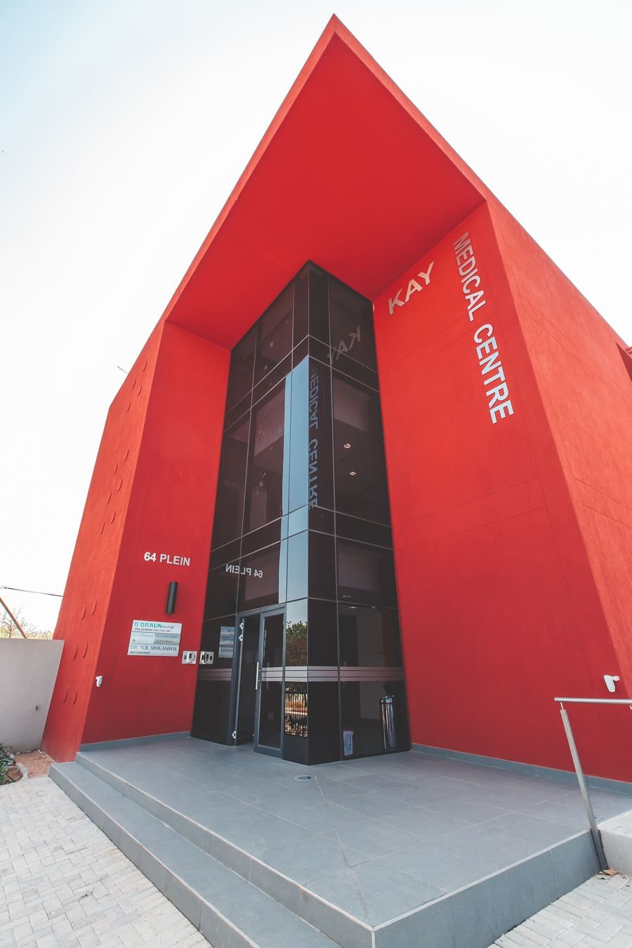 Entrance of the medical centre: a red angular volume with a glazed lift and stair core and the building name.