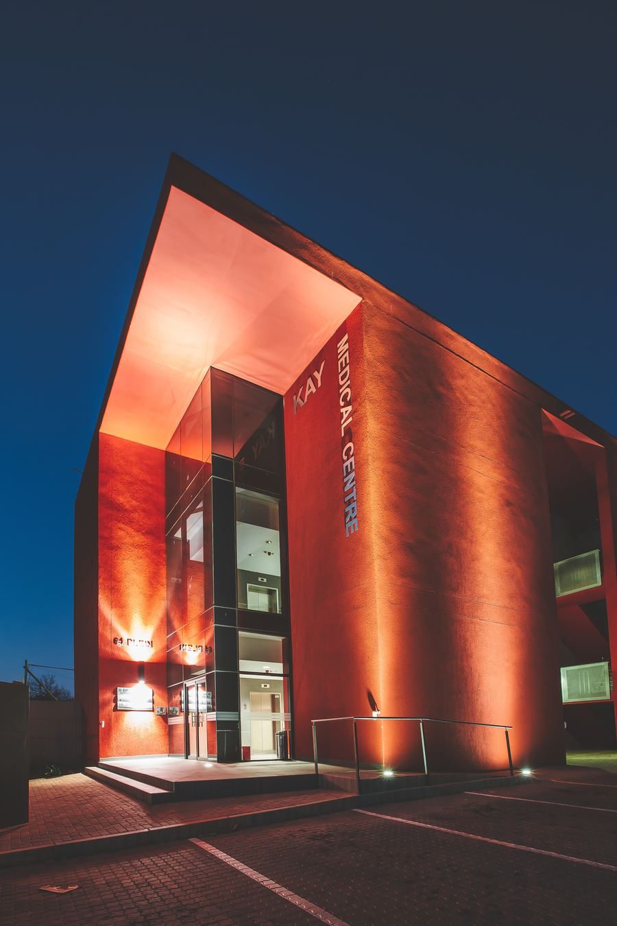 The medical centre at night, with its red walls and entrance canopy lit from below.