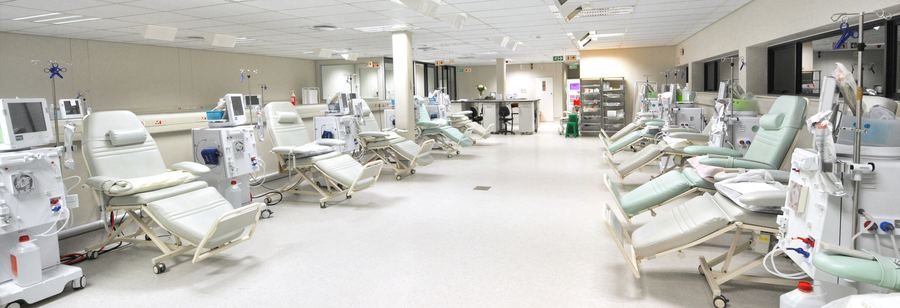 Dialysis unit with a row of treatment chairs and clinical equipment in a bright open ward.