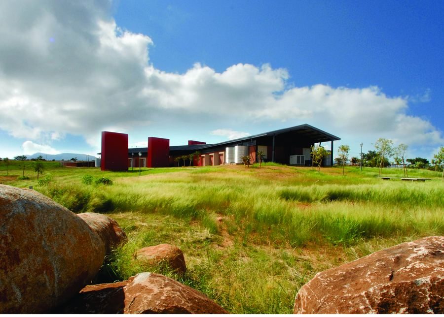 Library building with red face-brick tower elements and a low roof, set in open grassland beside large boulders.