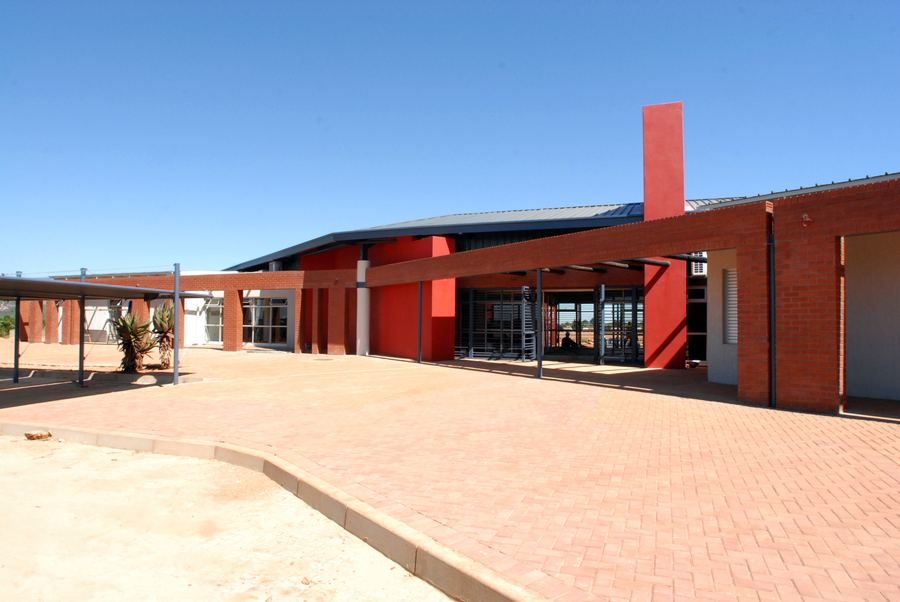 Library entrance forecourt with face-brick walls, a red tower element and a paved approach.