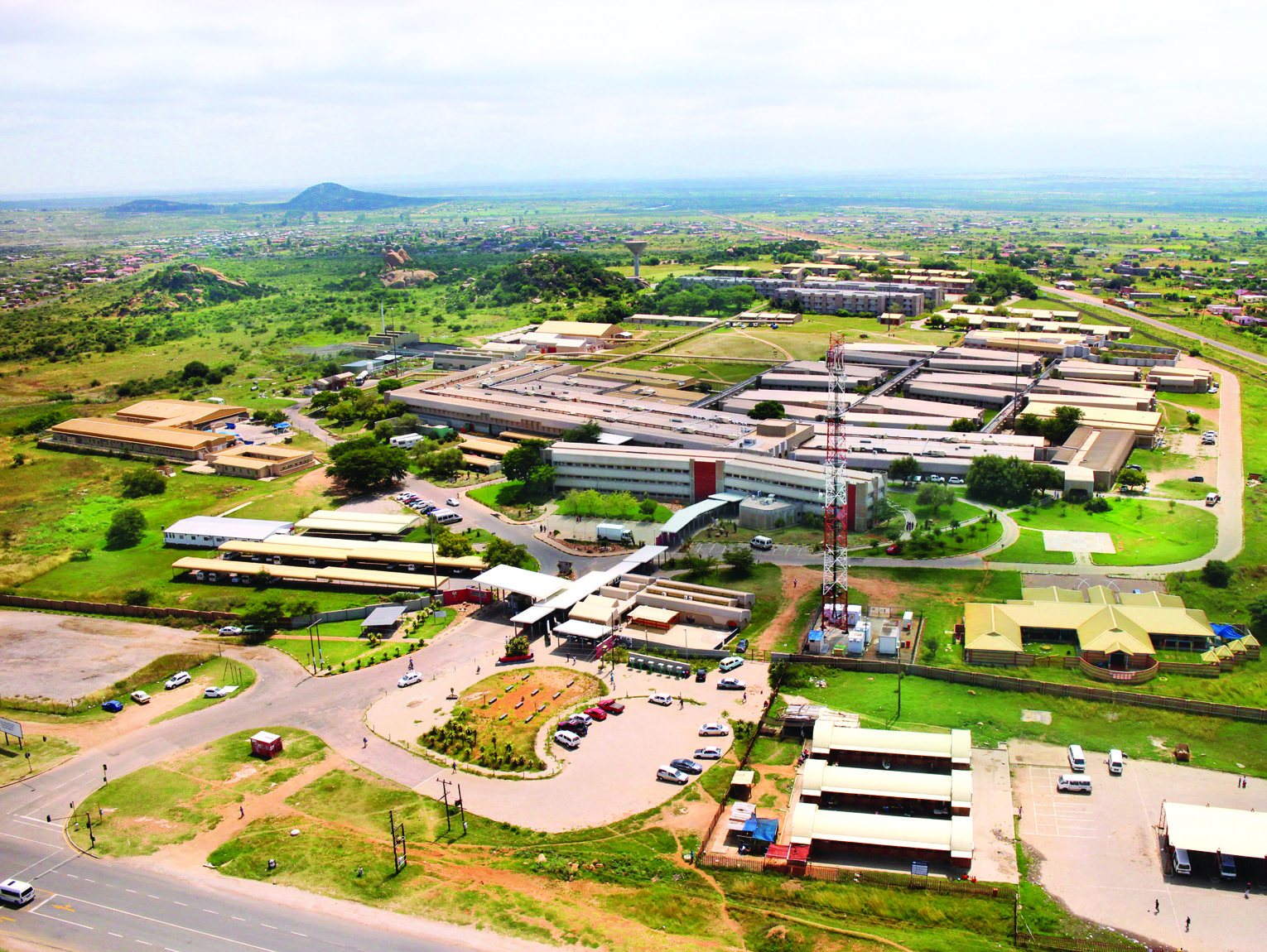 Aerial view of the hospital campus, with long ward and clinical blocks, access roads and surrounding landscape.