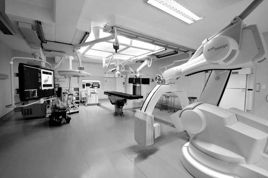 Theatre interior seen from the side, with the imaging arm, surgical pendants and a wall of monitors.