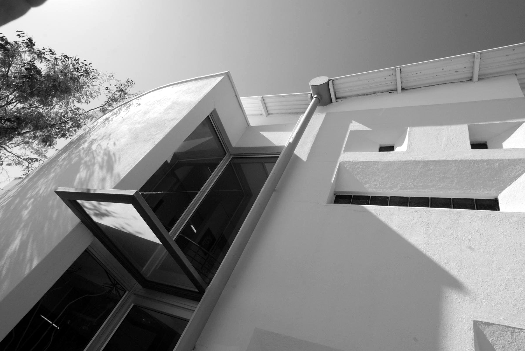 Corner of a white rendered office building with an angled glazed bay and projecting canopy, seen from below against the sky.
