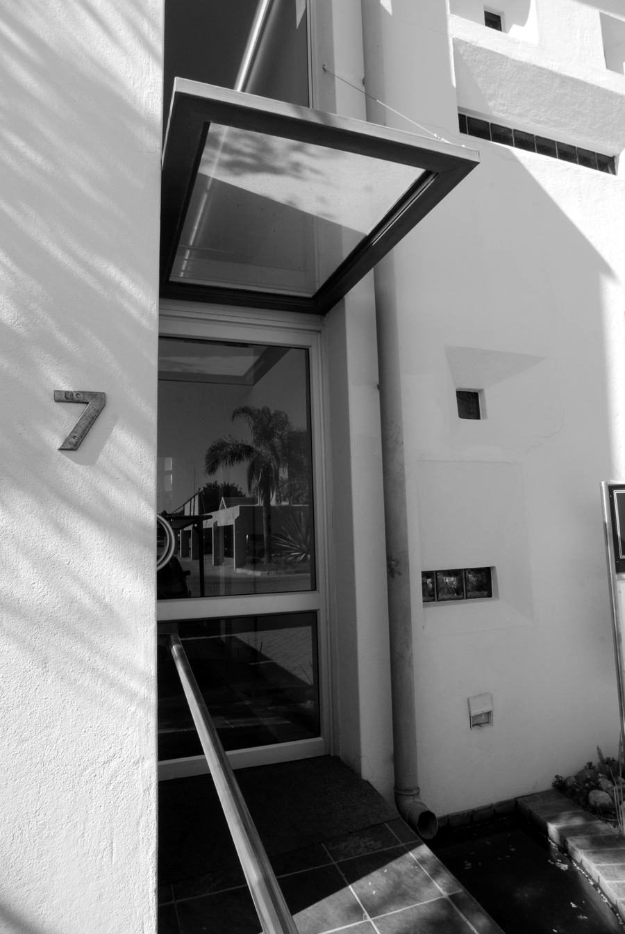 Entrance of the office building with a glass canopy, a steel handrail and the number 7 on the wall.