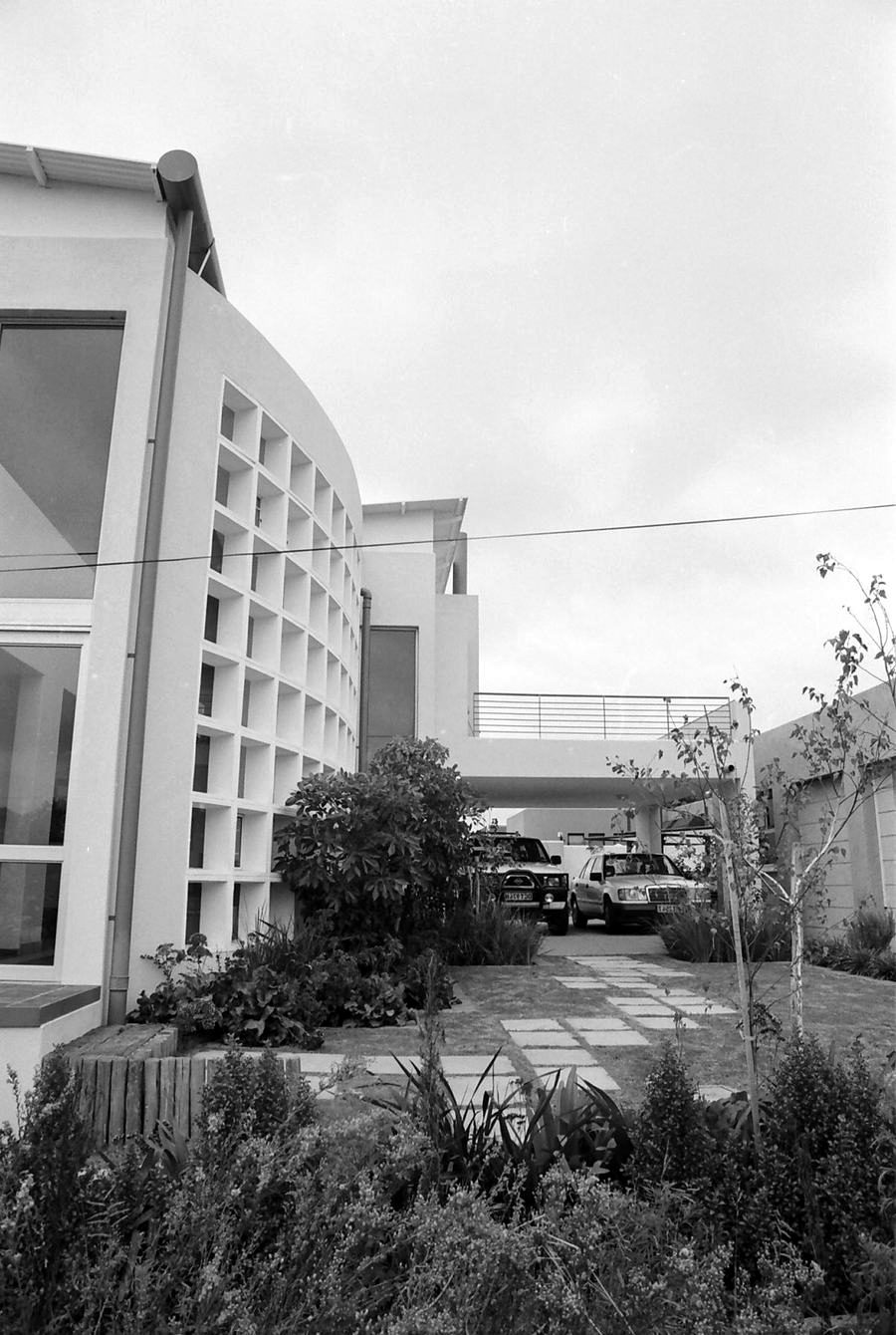 Rendered office building with a curved facade and a perforated screen wall, seen across a garden.
