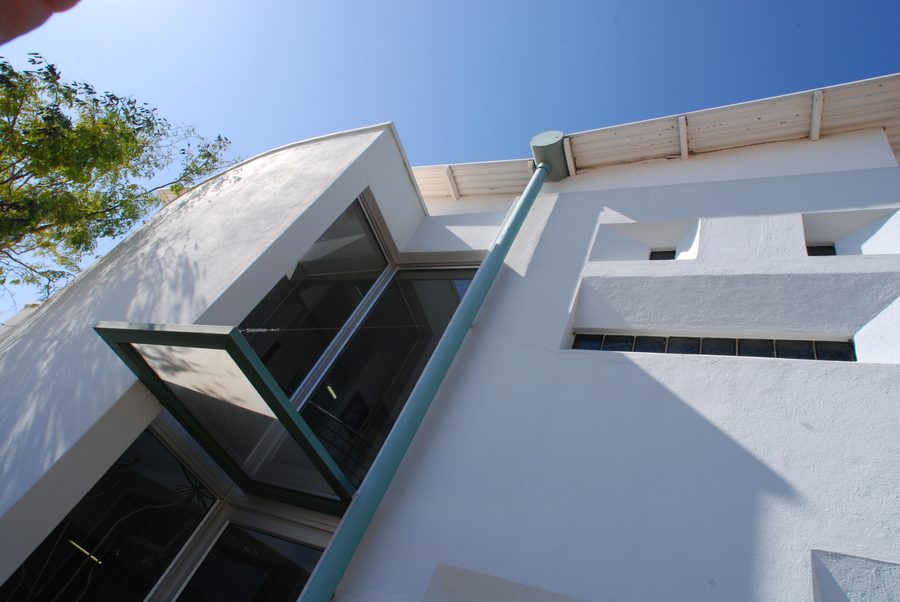 Curved white rendered corner of the office building with an angled glazed bay, seen from below against a blue sky.