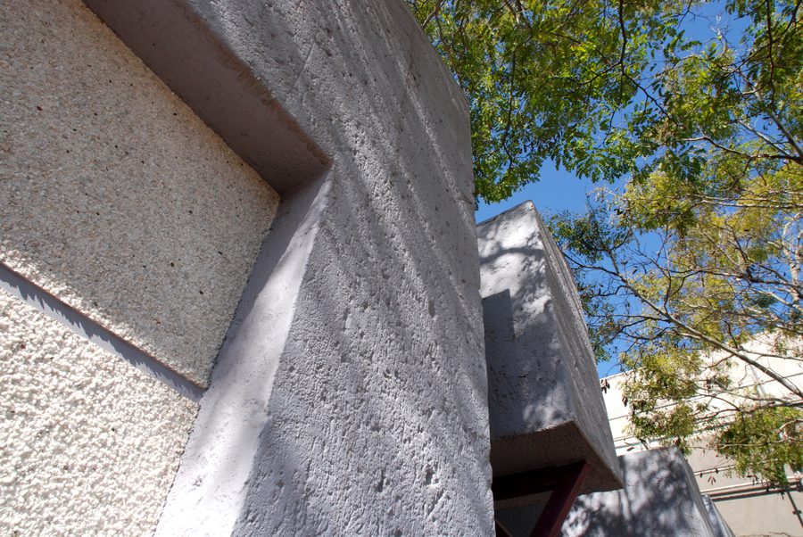 Textured plastered wall and recess, seen from close below with tree foliage behind.