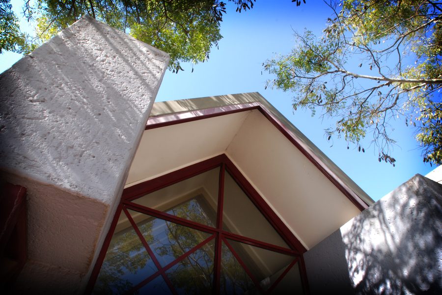 Pitched glazed gable with a red steel frame, seen from below against the sky.