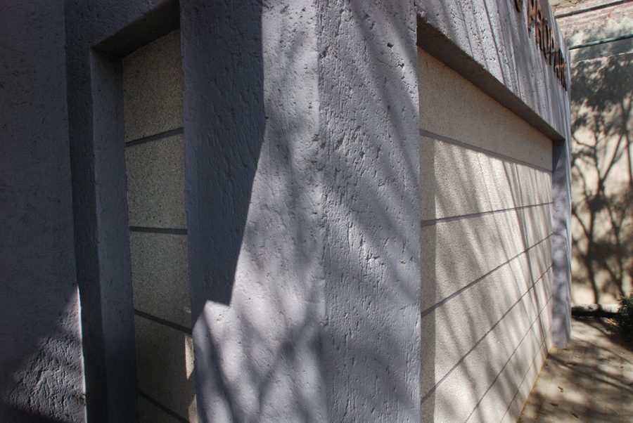 Grooved plastered wall with a narrow window opening, in dappled shade.
